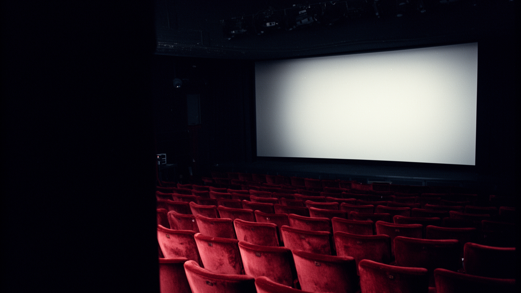 Cabine de projection calme avant la séance : faisceau allumé au-dessus des rangées de fauteuils vides d'une petite salle de cinéma.